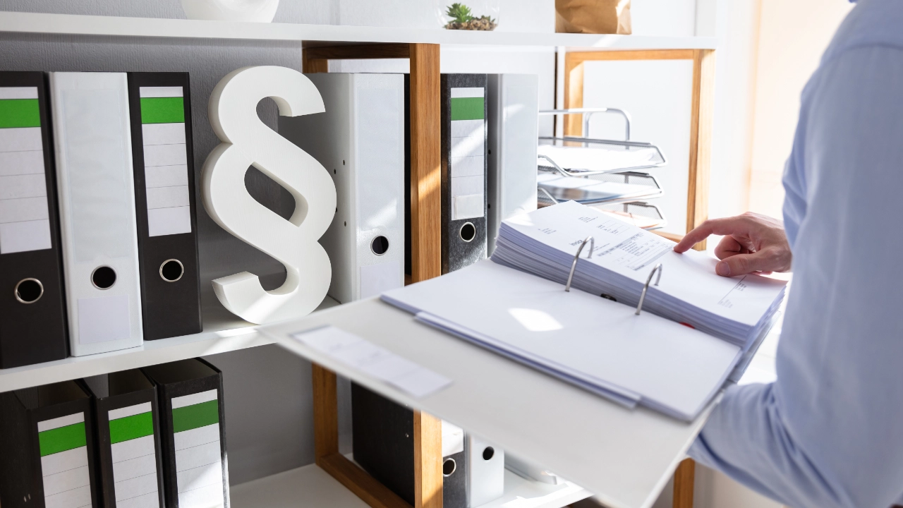 Mann steht im Büro und öffnet Ordner, Klausel im Regal im Hintergrund